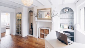 A modern interior with a wooden floor, white walls, a laptop on a desk, and a mirror above a shelf with glassware. - The Old Store Guest House (Chichester)