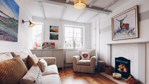 A cozy living room with a fireplace, a sofa set, and a dining area with a view of the outdoors. - The Old Store Guest House (Chichester)