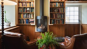 A cozy living room with leather chairs, a fireplace, and bookshelves filled with books. - The Turtley Corn Mill (South Brent)