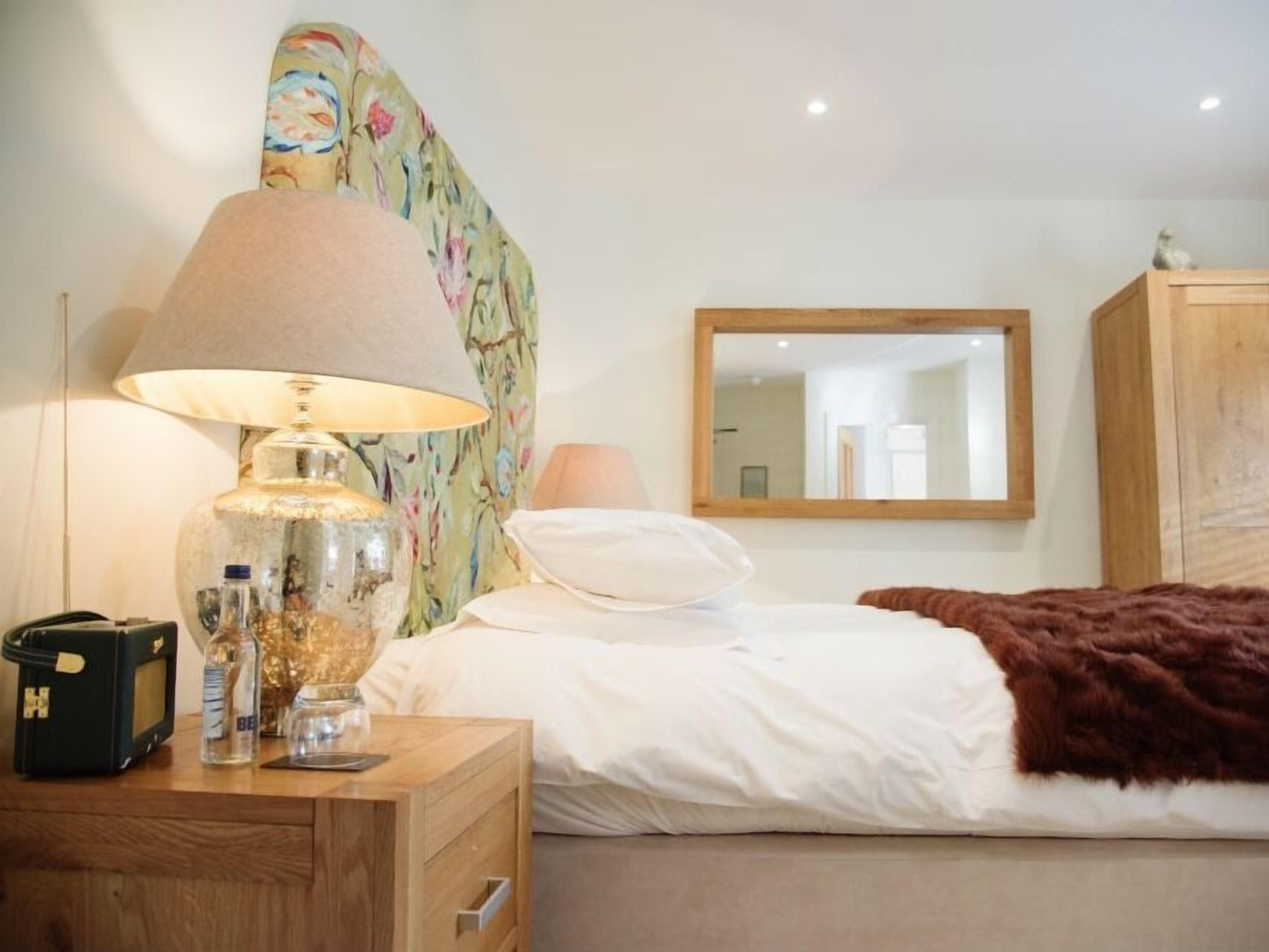 Ein Schlafzimmer mit Bett, Nachttisch aus Holz, Lampe, Spiegel und Kleiderschrank.