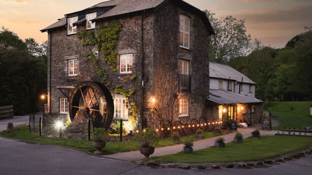 A stone building with a large water wheel, ivy on the walls, and outdoor lighting. - The Turtley Corn Mill (South Brent)