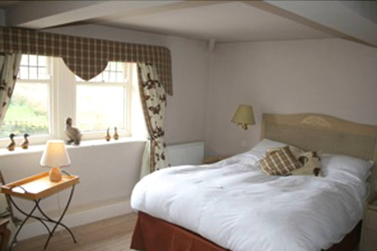 Une chambre à coucher comprenant un lit, une table de chevet, une lampe, une fenêtre avec des rideaux et une vue sur l’extérieur.