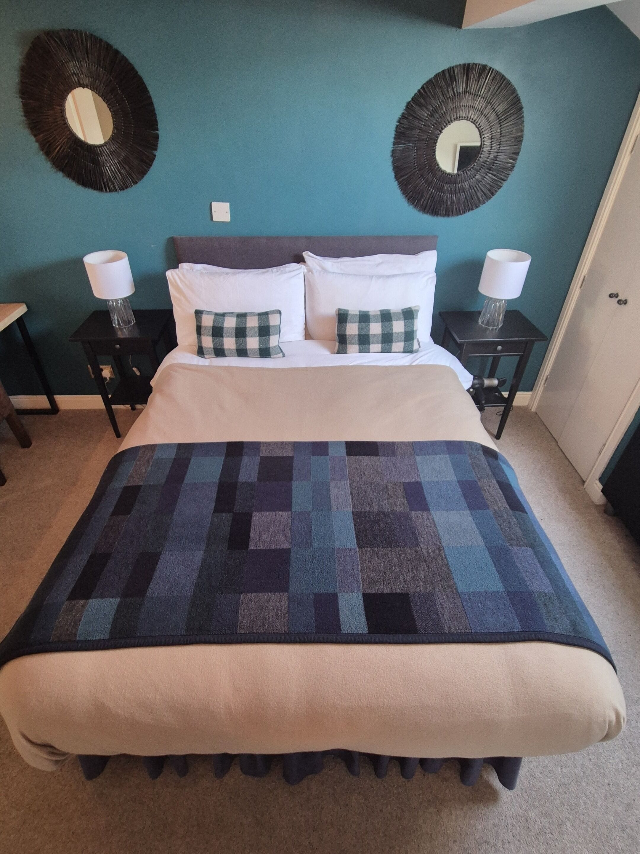 A bed with a checkered blanket, two pillows, and two bedside tables with lamps.