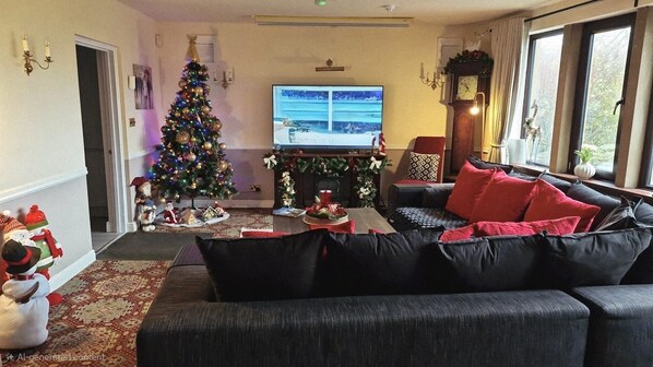 A cozy living room with a large black sofa, a Christmas tree, and a fireplace.
