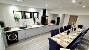 Una cocina moderna con lavavajillas incorporado, una mesa de comedor grande para seis personas y un rincón de estar con sillas azules.