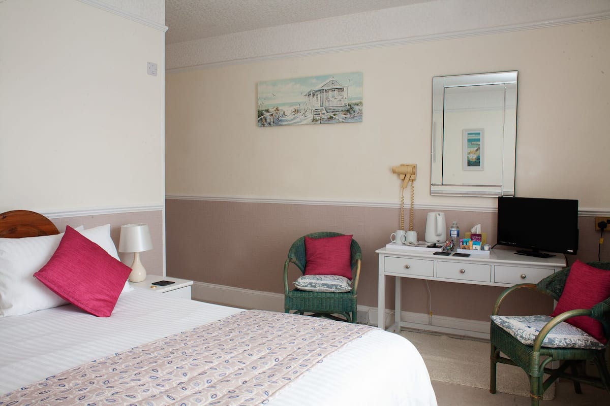 A hotel room with a bed, a desk, a chair, a television, and a painting on the wall.