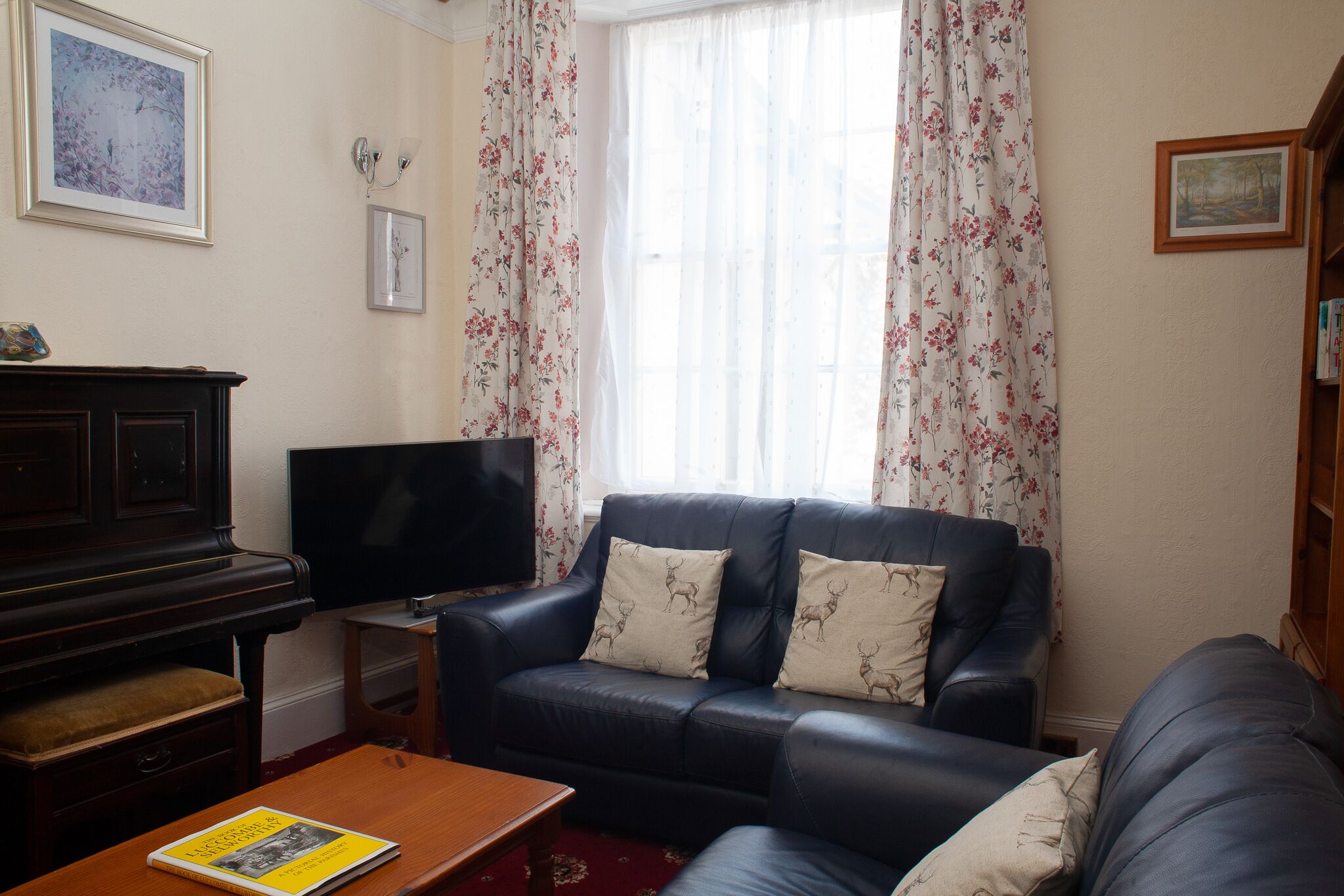A living room with a dark blue sofa, a wooden coffee table, a television, and a piano.