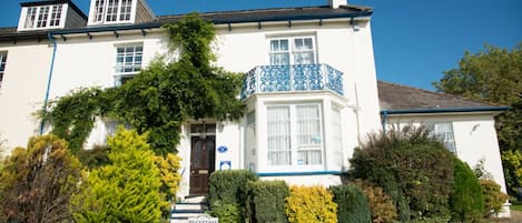 A white building with a blue balcony, a reception sign, and well-maintained gardens.