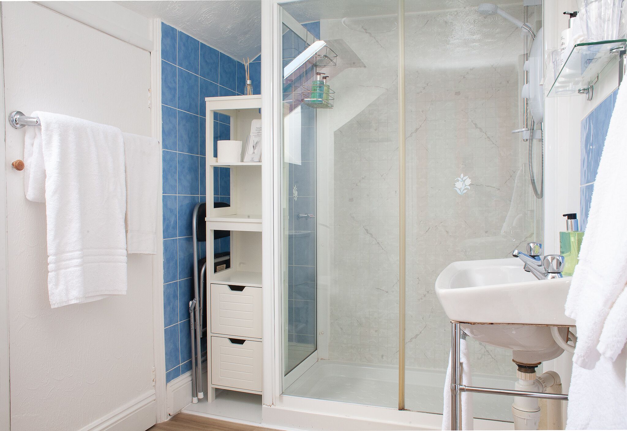 A bathroom with a glass-enclosed shower, a white sink, and blue tiles.