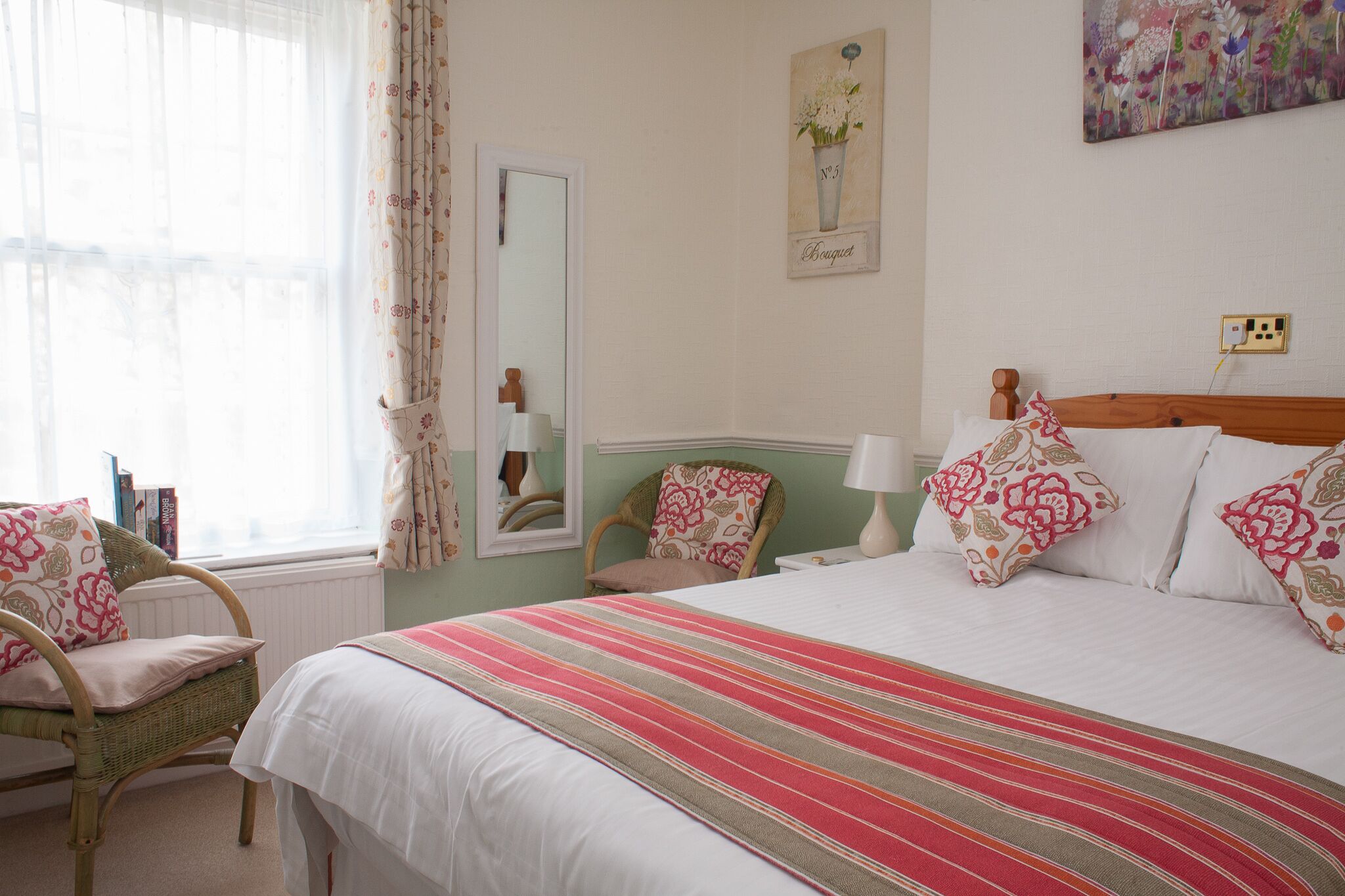 Een slaapkamer met een bed, een stoel, een spiegel en een schilderij aan de muur.