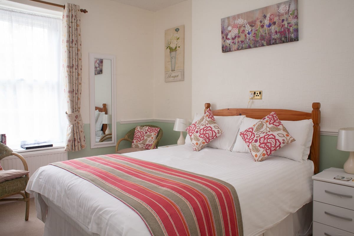 A neatly arranged bedroom with a large bed, two bedside tables, a chair, and a window with curtains.