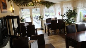 A restaurant with wooden tables and chairs, a chandelier, and greenery on the walls.