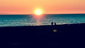 A sunset over the ocean with two silhouettes of people standing on the beach.