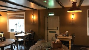 A cozy restaurant interior with wooden tables and chairs, pendant lighting, and a visible exit door. - The Swan Hotel Smoke & Taphouse (Telford)