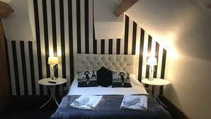 A hotel room with a tufted headboard, two bedside tables with lamps, a bed with a dark blue bedspread, and a striped wall design. - The Swan Hotel Smoke & Taphouse (Telford)