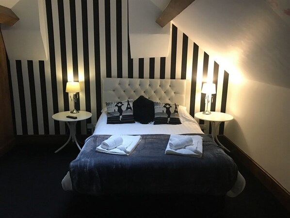 A hotel room with a tufted headboard, two bedside tables with lamps, a bed with a dark blue bedspread, and a striped wall design.