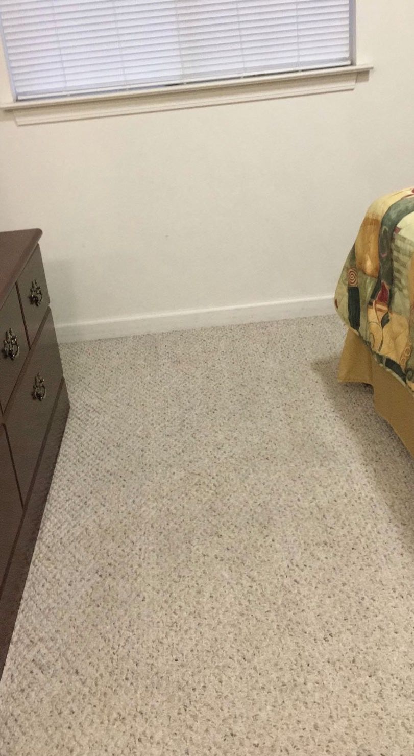 Una habitación con piso alfombrado, un aparador de madera y una cama con manta estampada.