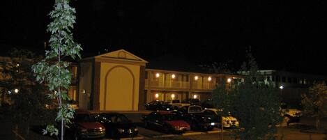 A building with a central arched entrance, surrounded by a parking lot with several cars.