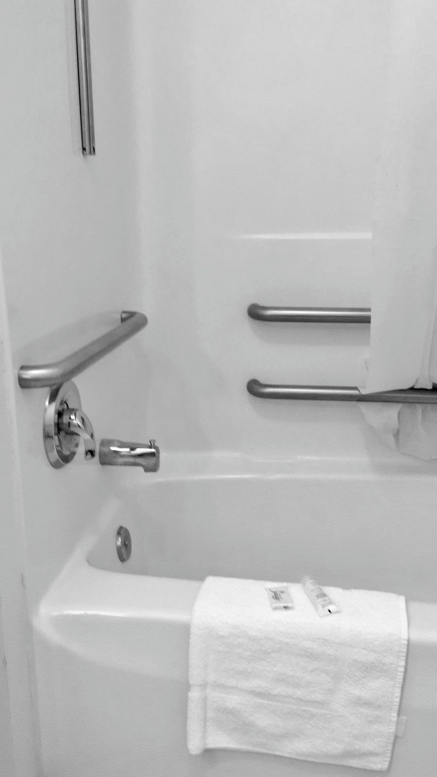 A bathroom with a bathtub, a towel, and a handrail.
