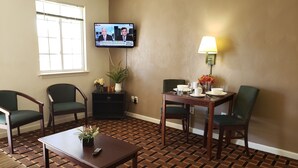 A hotel room with a TV mounted on the wall, a dining table with chairs, a lamp, and a patterned carpet. - Affordable Suites Burlington (Burlington)