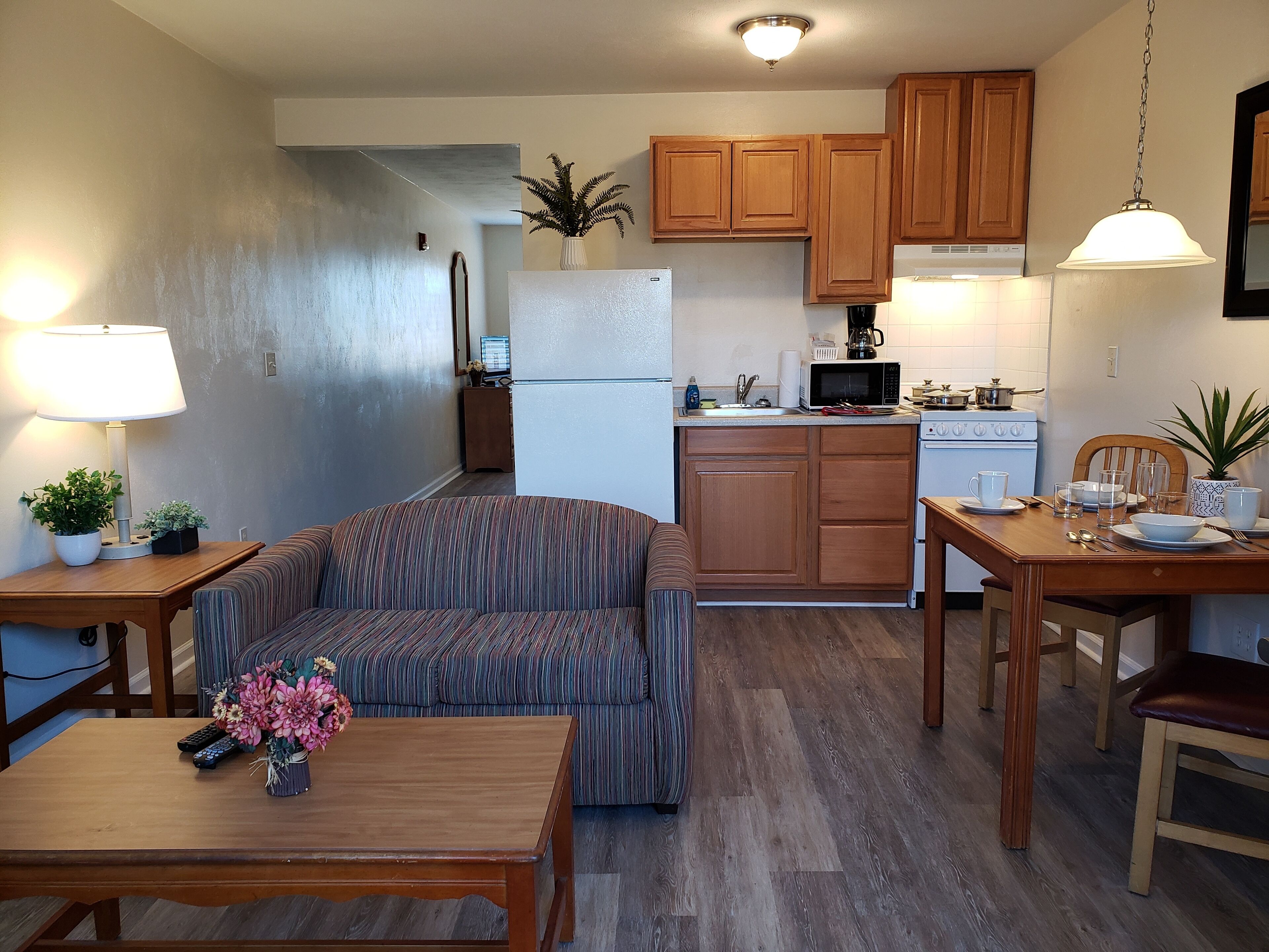 A compact living space with a kitchenette, a sofa, a dining table, and a lamp.