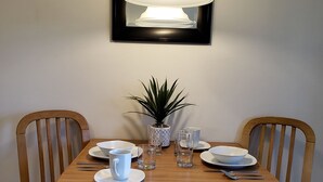 A dining table set with plates, bowls, glasses, and cutlery, flanked by wooden chairs, under a hanging light fixture. - Affordable Suites Burlington (Burlington)