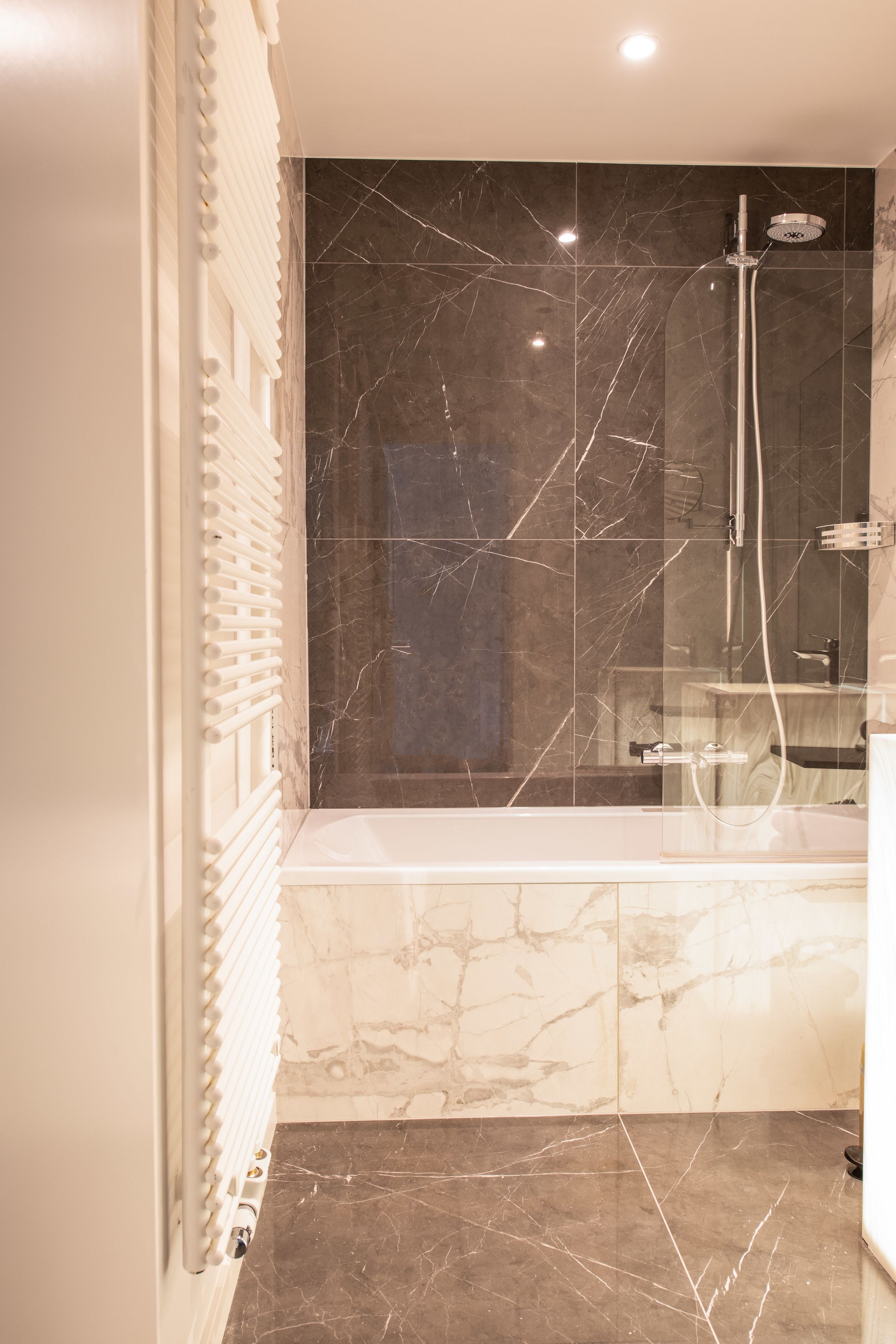 Une salle de bain avec une baignoire, un espace de douche clos par des parois de verre et des murs en marbre.
