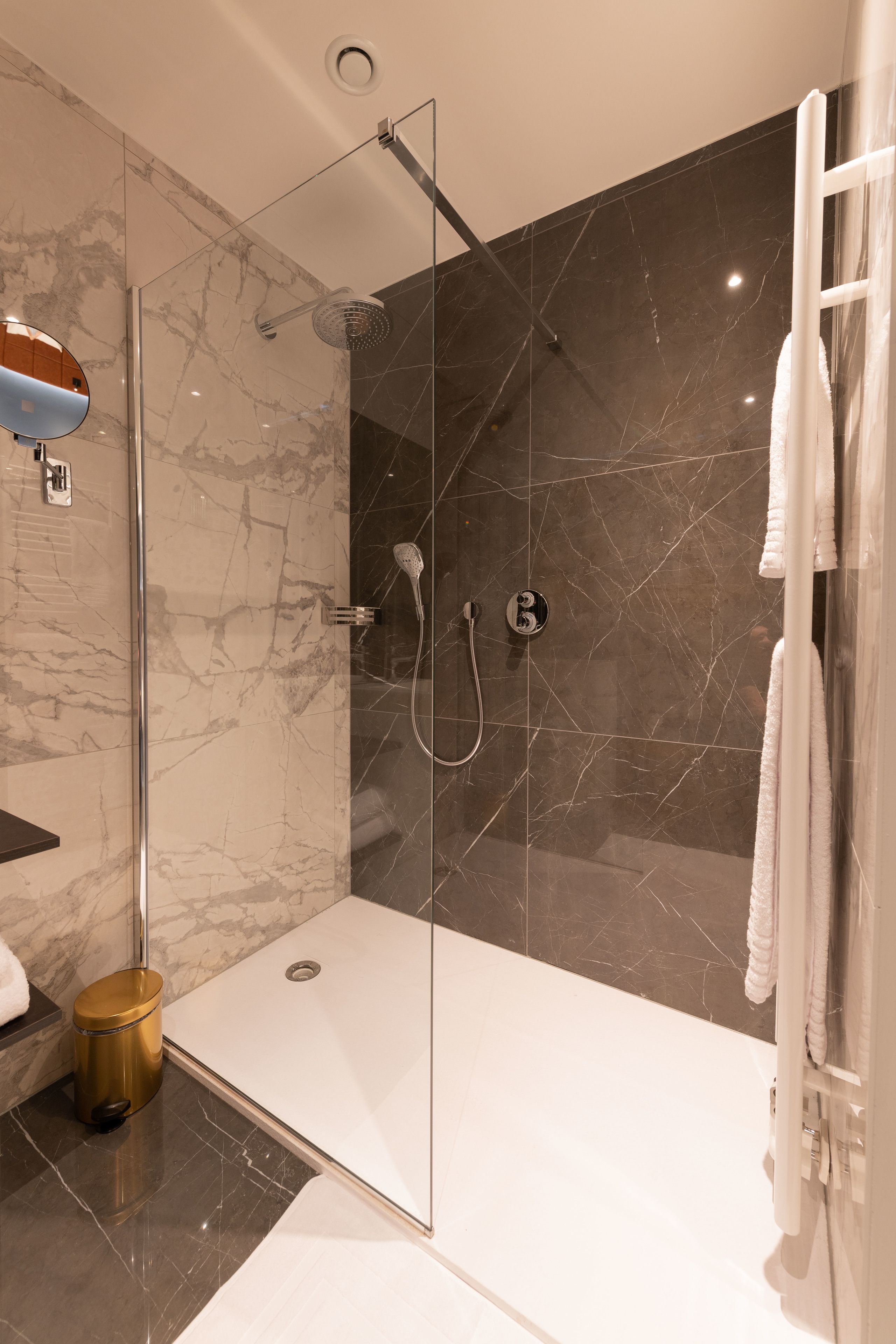 Un bagno moderno con doccia vetrata, pareti in marmo e vasca da bagno bianca.