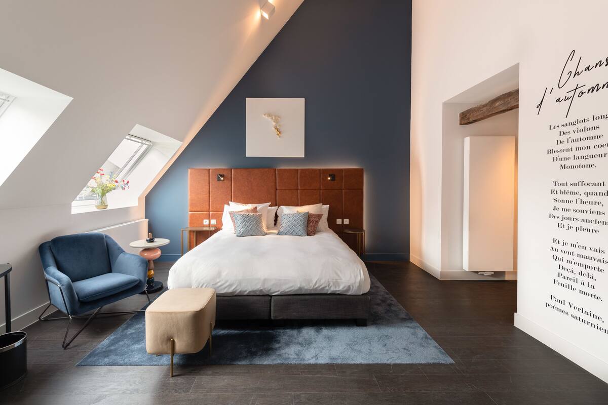 Ein modernes Schlafzimmer mit einem großen Bett, einem blauen Sessel, einem kleinen Tisch und einer dekorativen Wandgestalt.