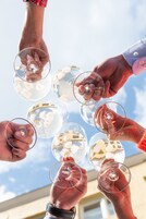 Manos sosteniendo copas de vino contra un cielo despejado.