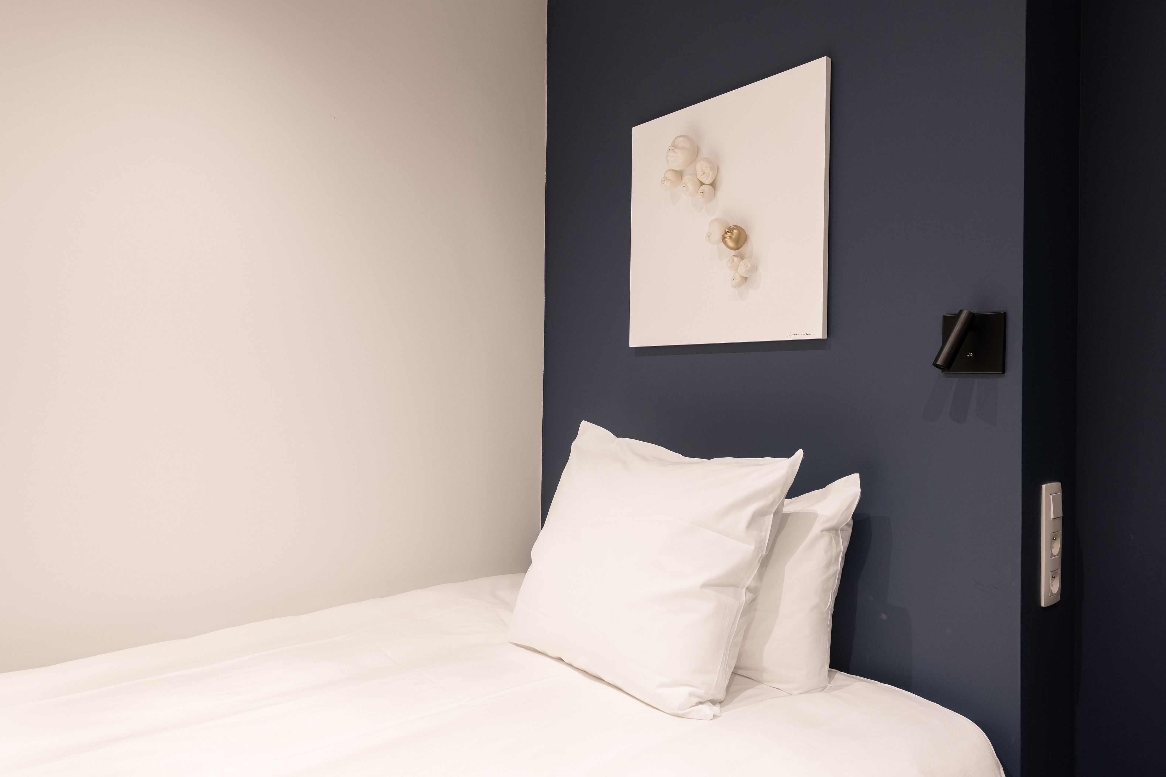 Una cama bien hecha con ropa blanca en una habitación con un revestimiento azul oscuro.