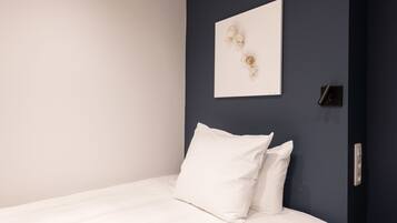 Una cama bien hecha con ropa blanca en una habitación con un revestimiento azul oscuro.