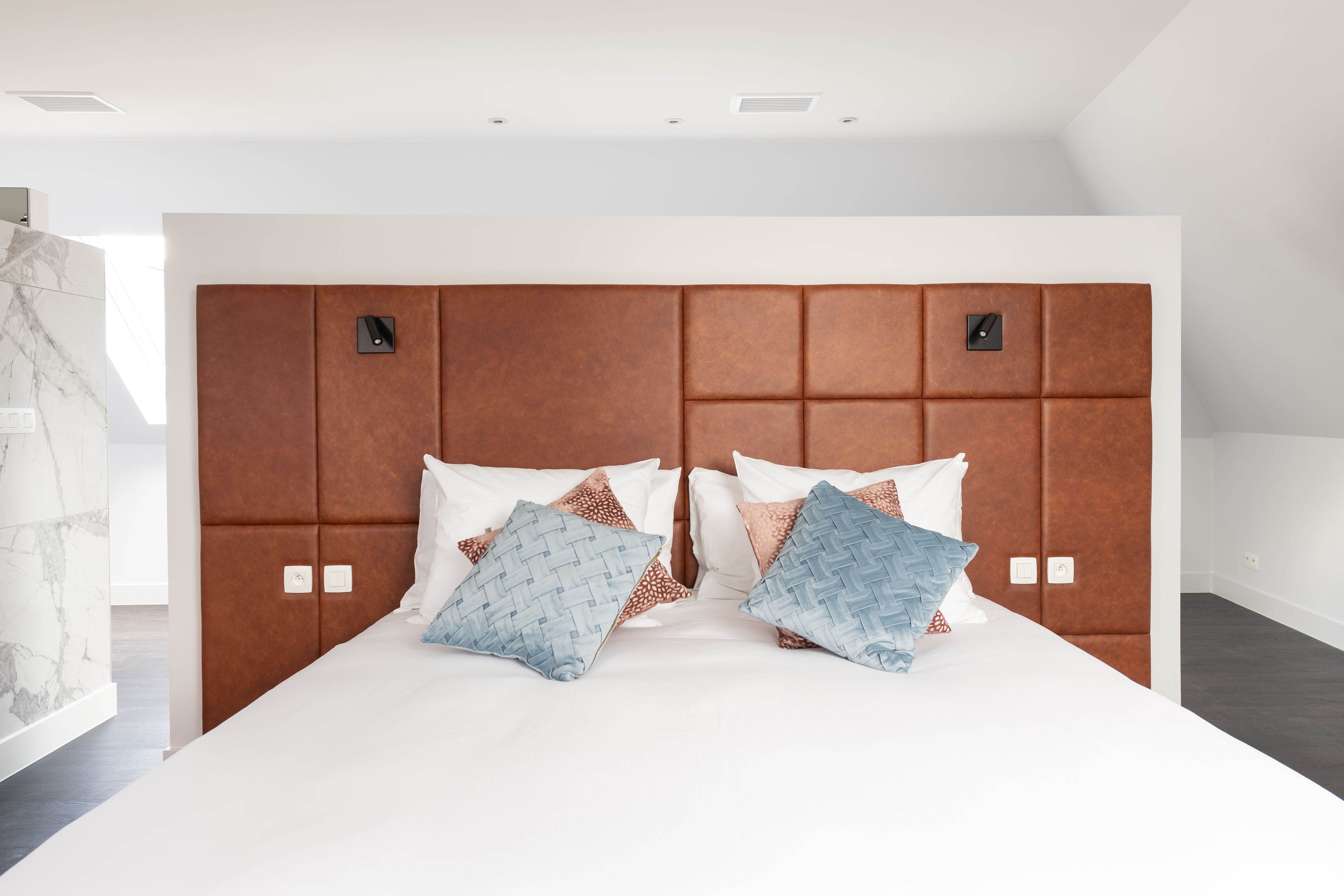 A modern hotel room with a large bed, a wooden headboard, and a marble accent wall.