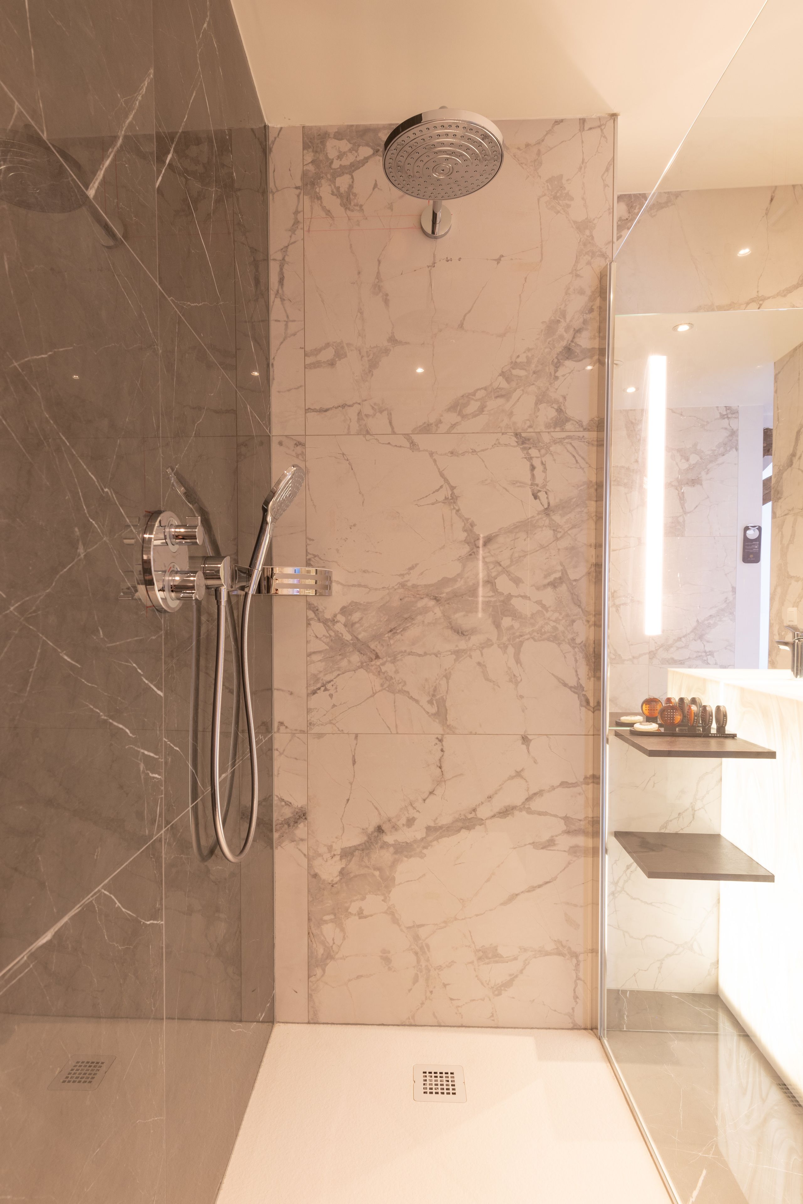 A modern bathroom with a shower, marble walls, and a glass partition.