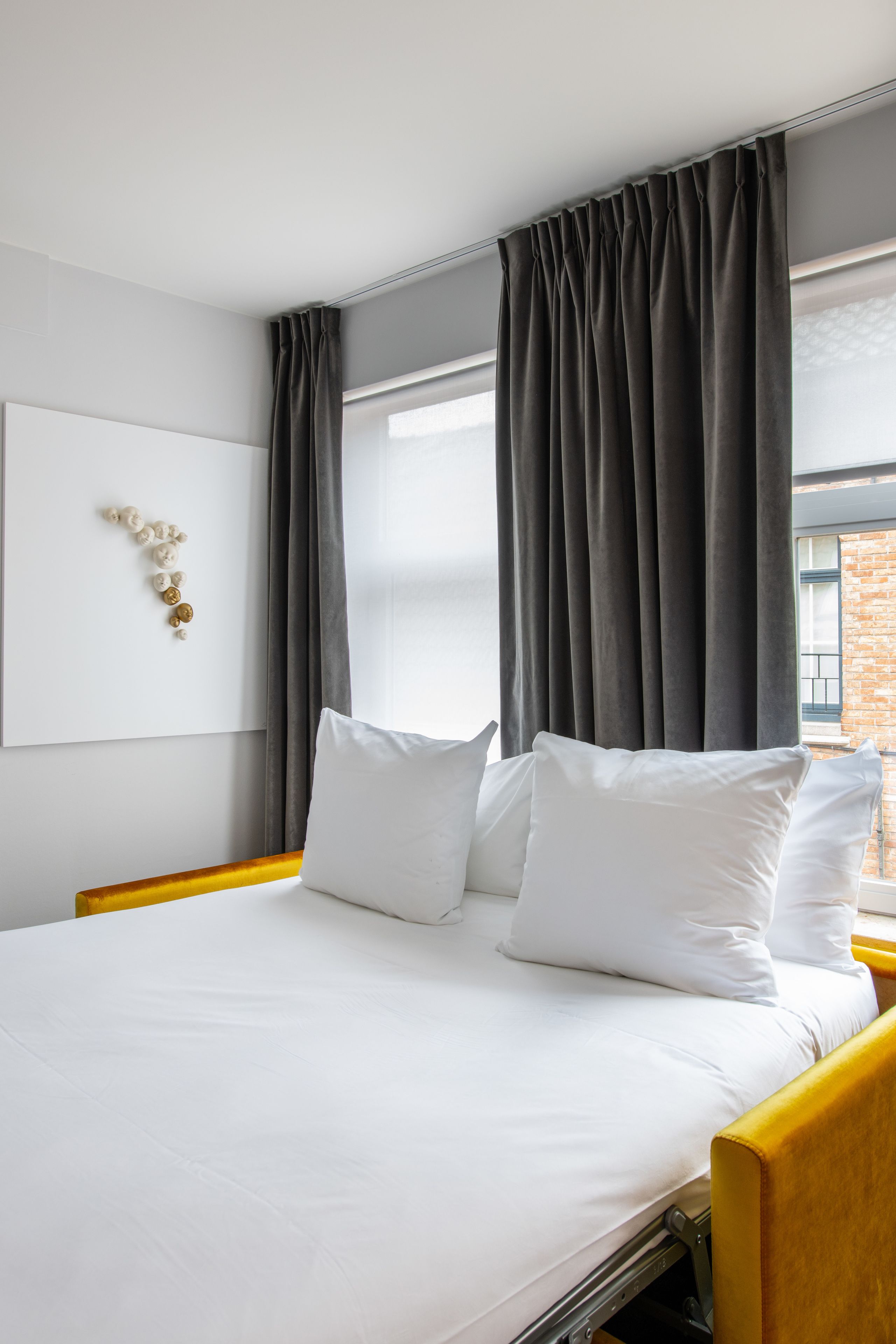 Een hotelkamer met een bed, wit beddengoed, een hoofdbord, een raam met gordijnen en een decoratie aan de muur.