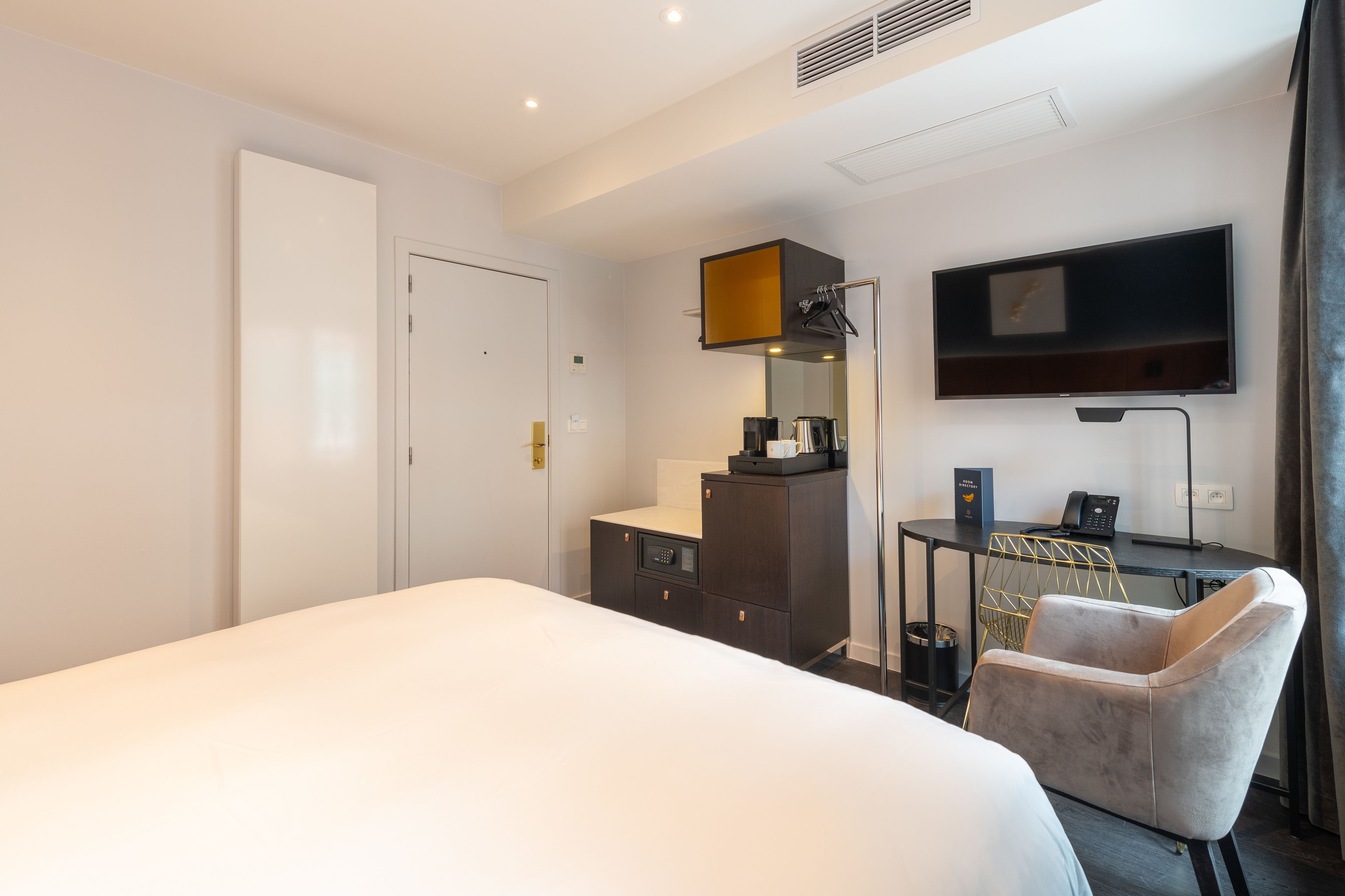 A hotel room with a bed, a desk with a chair, a television, and a wardrobe.