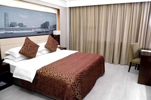 Camera d'albergo con un letto, una scrivania, una sedia, vista sulla città e una finestra con tende.