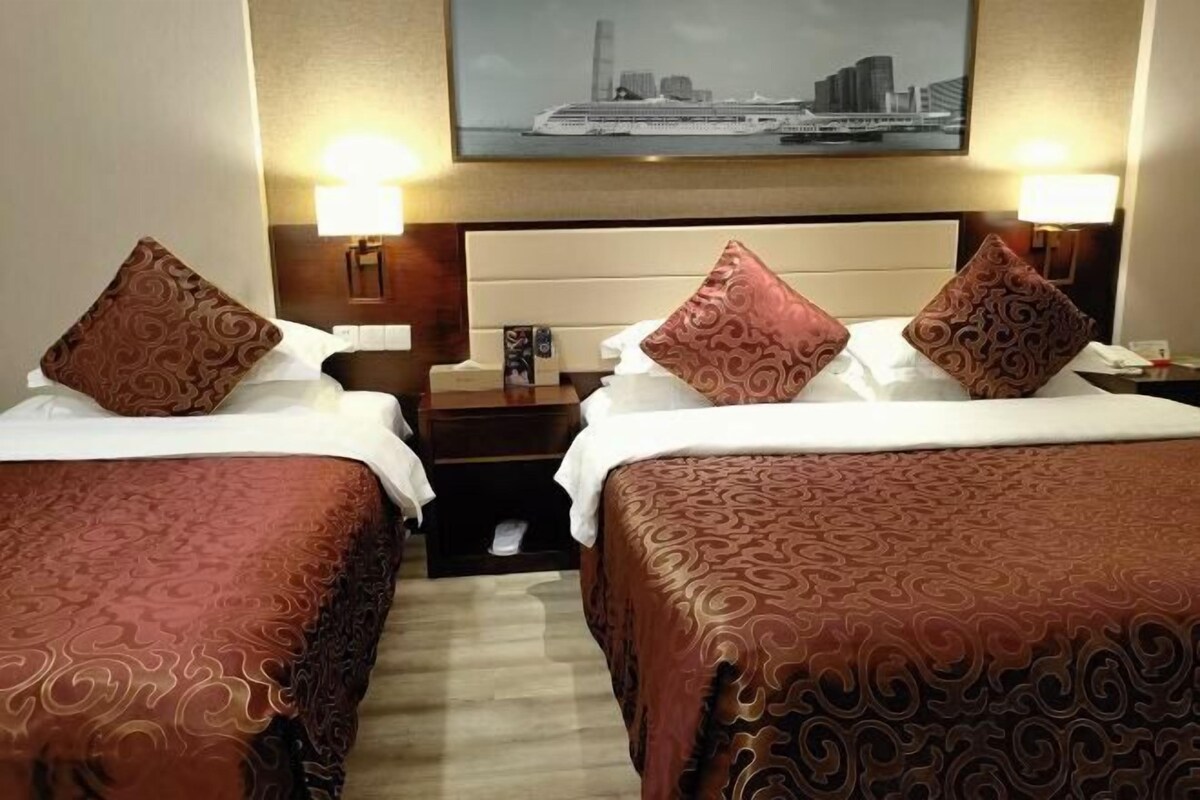 Camera d'albergo con due letti, ciascuno con copriletto e cuscini coordinati, un comodino con lampada e una fotografia incorniciata di una veduta cittadina.