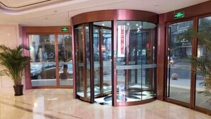 A revolving door with glass panels and a metallic frame, leading to an entrance with a green exit sign. - Hongluyuan Hotel (Shanghai)