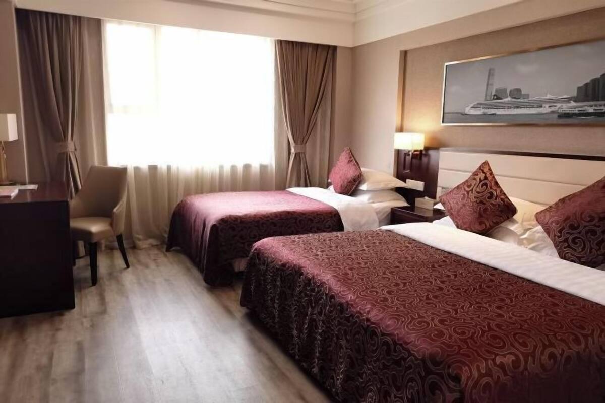 A hotel room with two beds, a desk, a chair, and a large window with curtains.