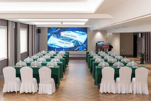 Un salón de conferencias con filas de mesas, sillas y una gran pantalla para presentaciones.