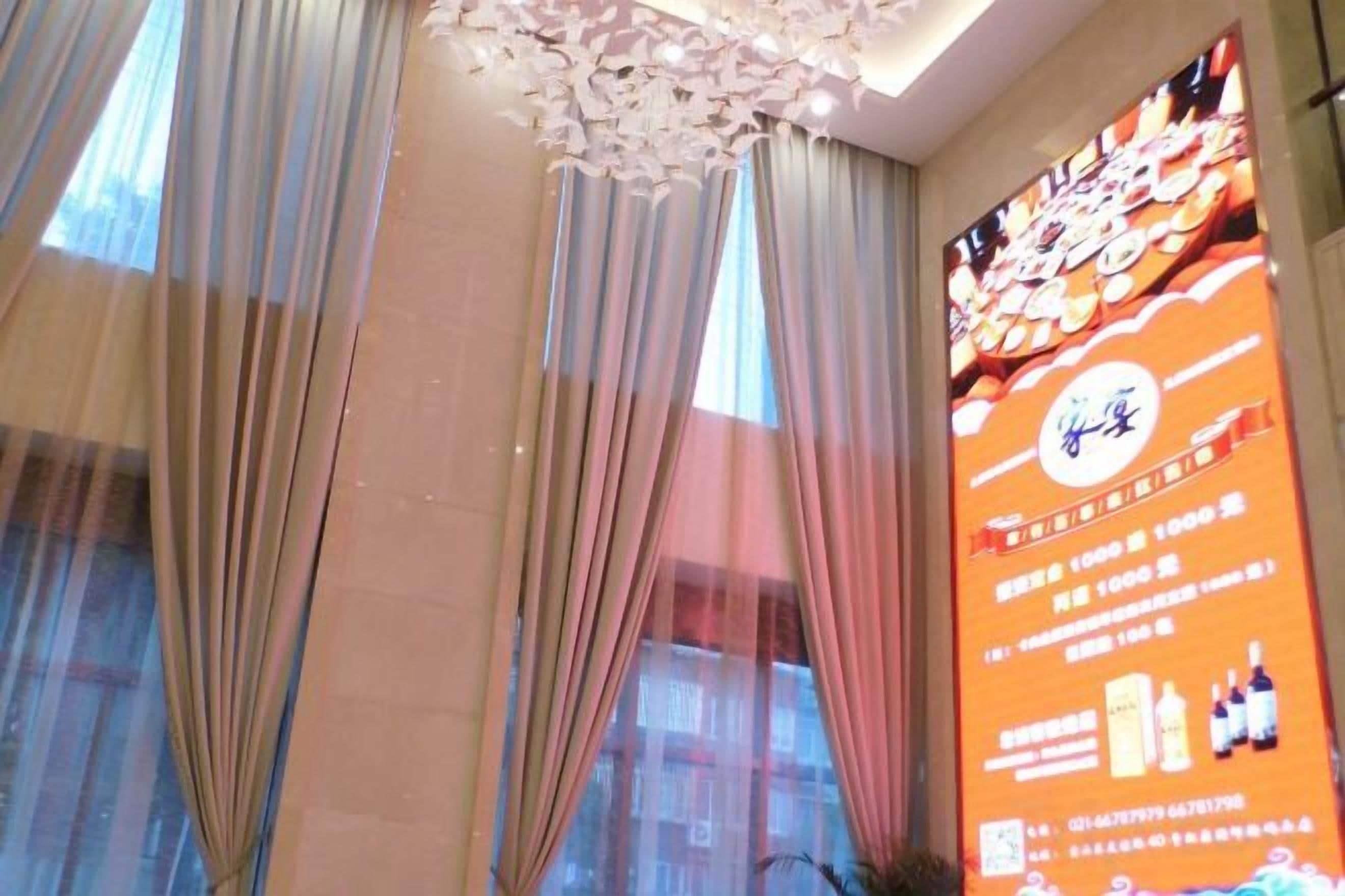 A hotel room with a large window, sheer curtains, and a ceiling light fixture.