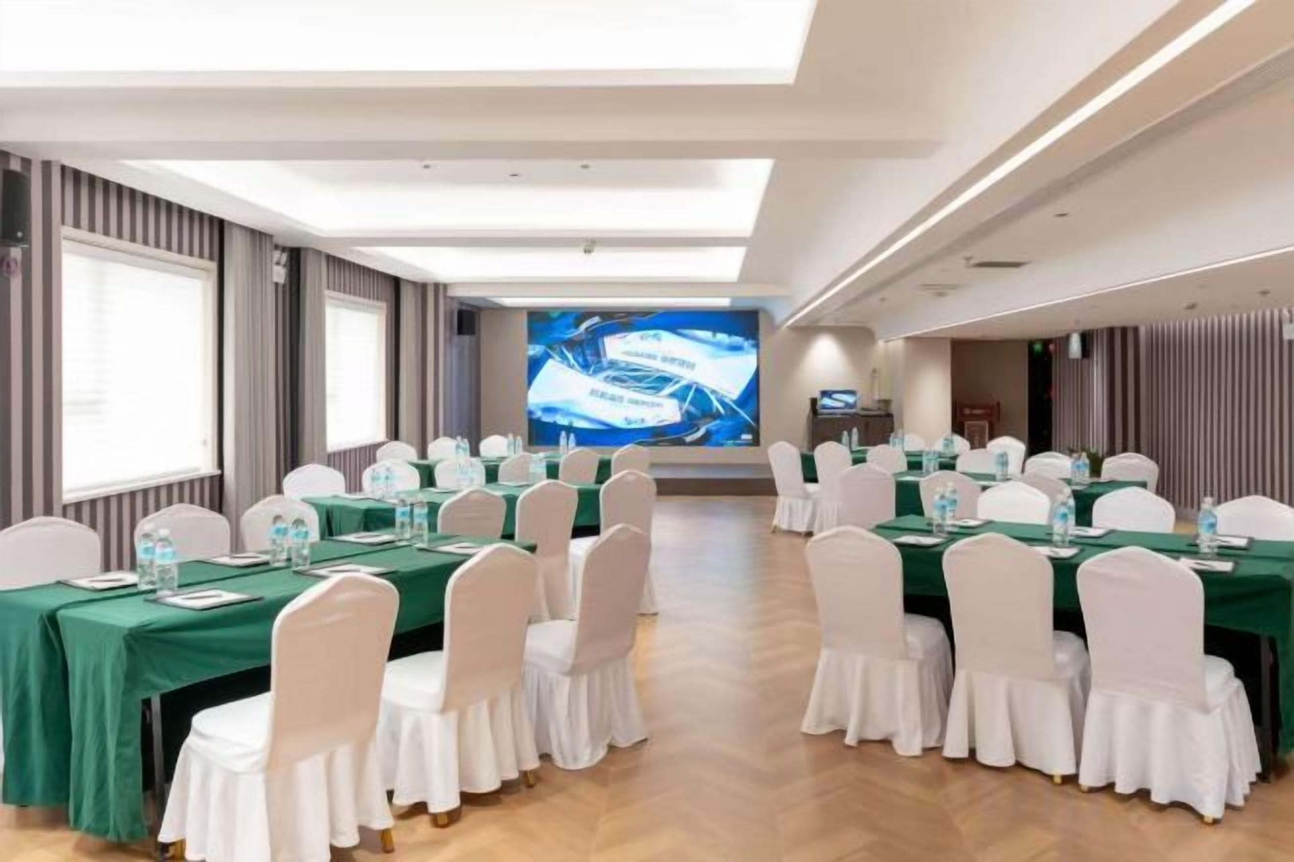 A conference room with round tables, white chairs, and a large screen at the front.