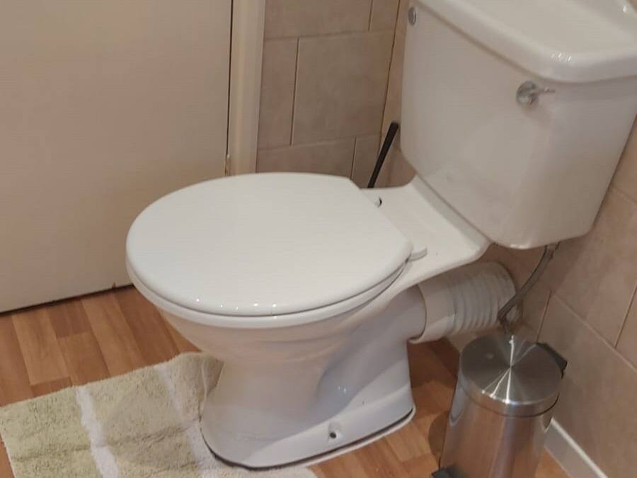 A bathroom with a toilet, a trash bin, and a floor mat.