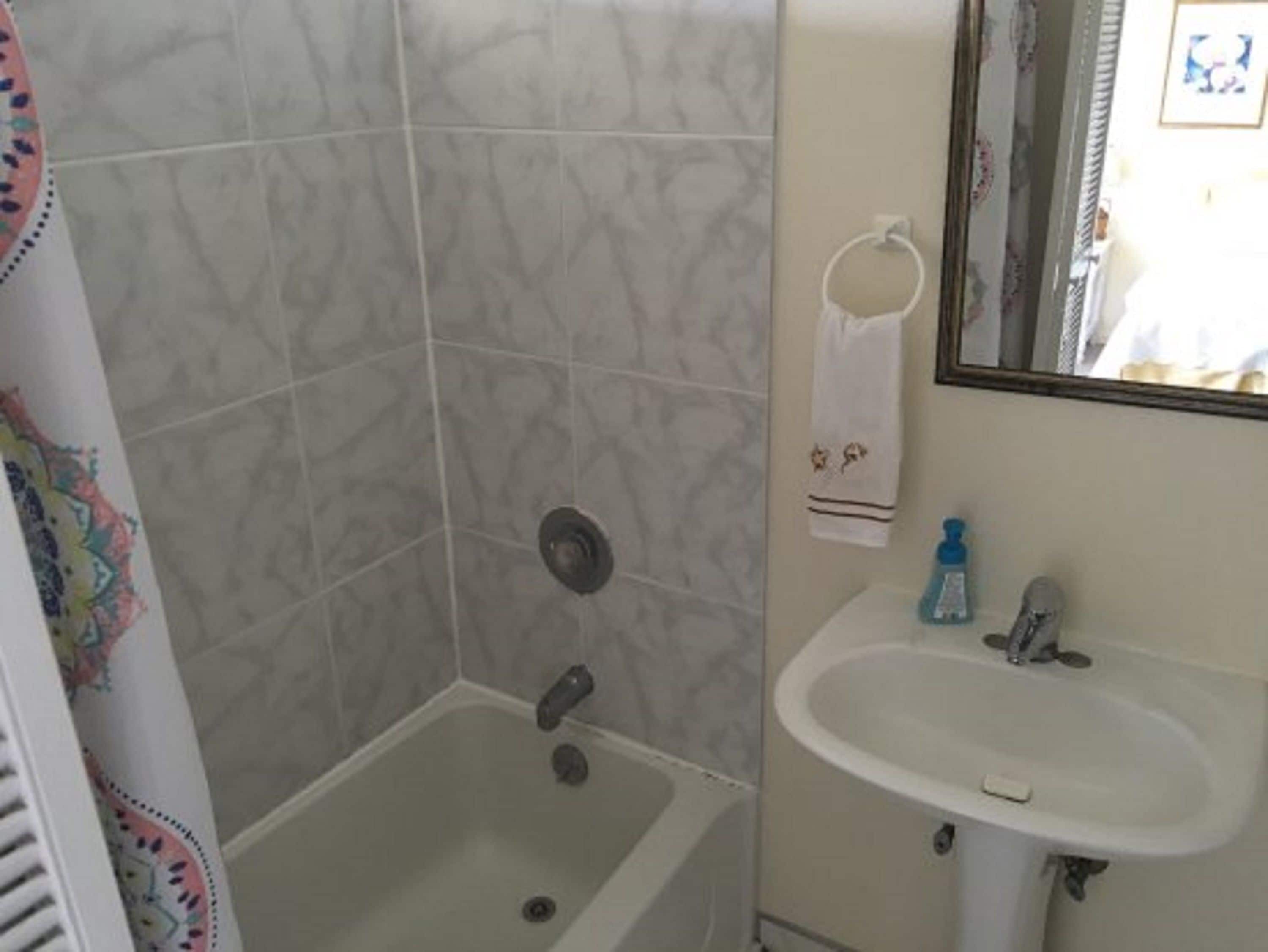 A bathroom with a shower, a sink, and a towel rack.