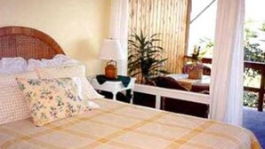 A bedroom with a bed, a nightstand, a lamp, and a view of the outdoors. - Hale-hoola B & B (Captain Cook)