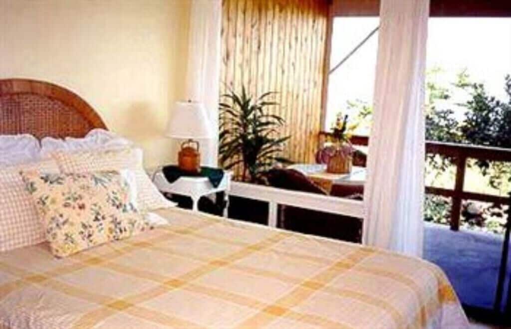 A bedroom with a bed, a nightstand, a lamp, and a view of the outdoors.