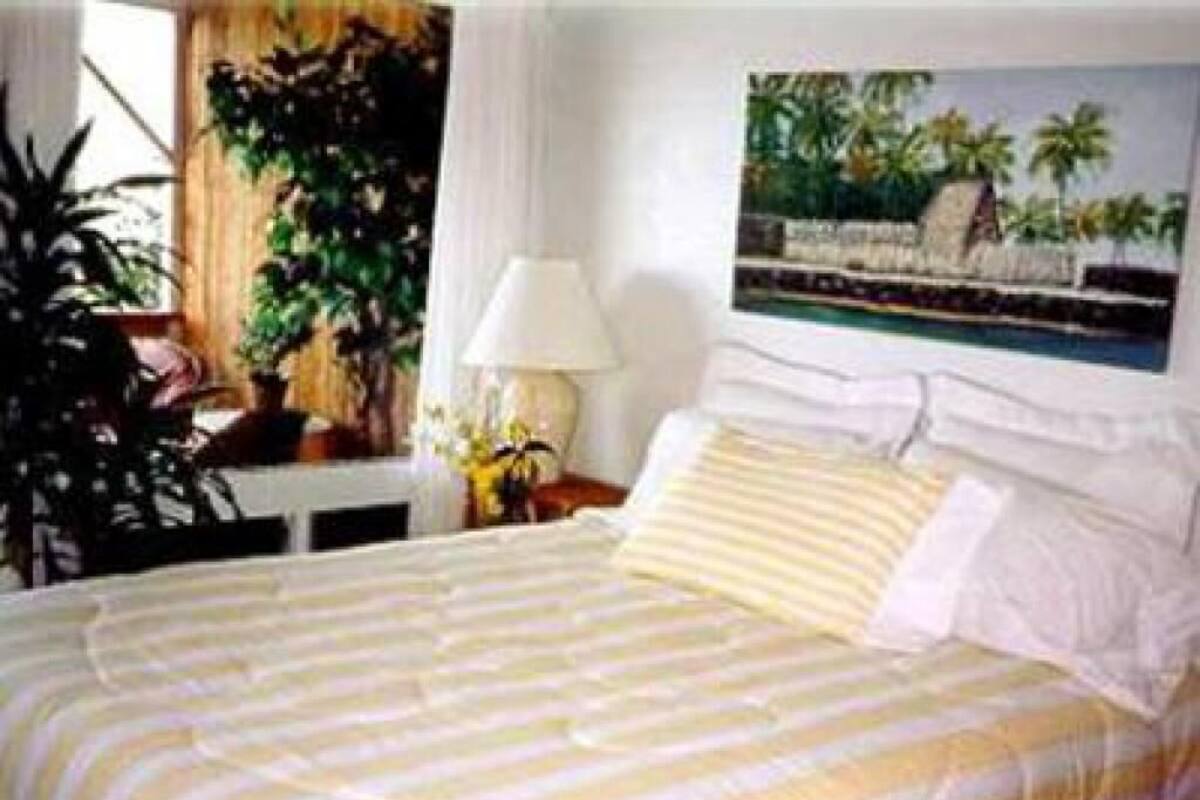 A bed with striped bedding, a nightstand with a lamp, and a painting of a beach scene.