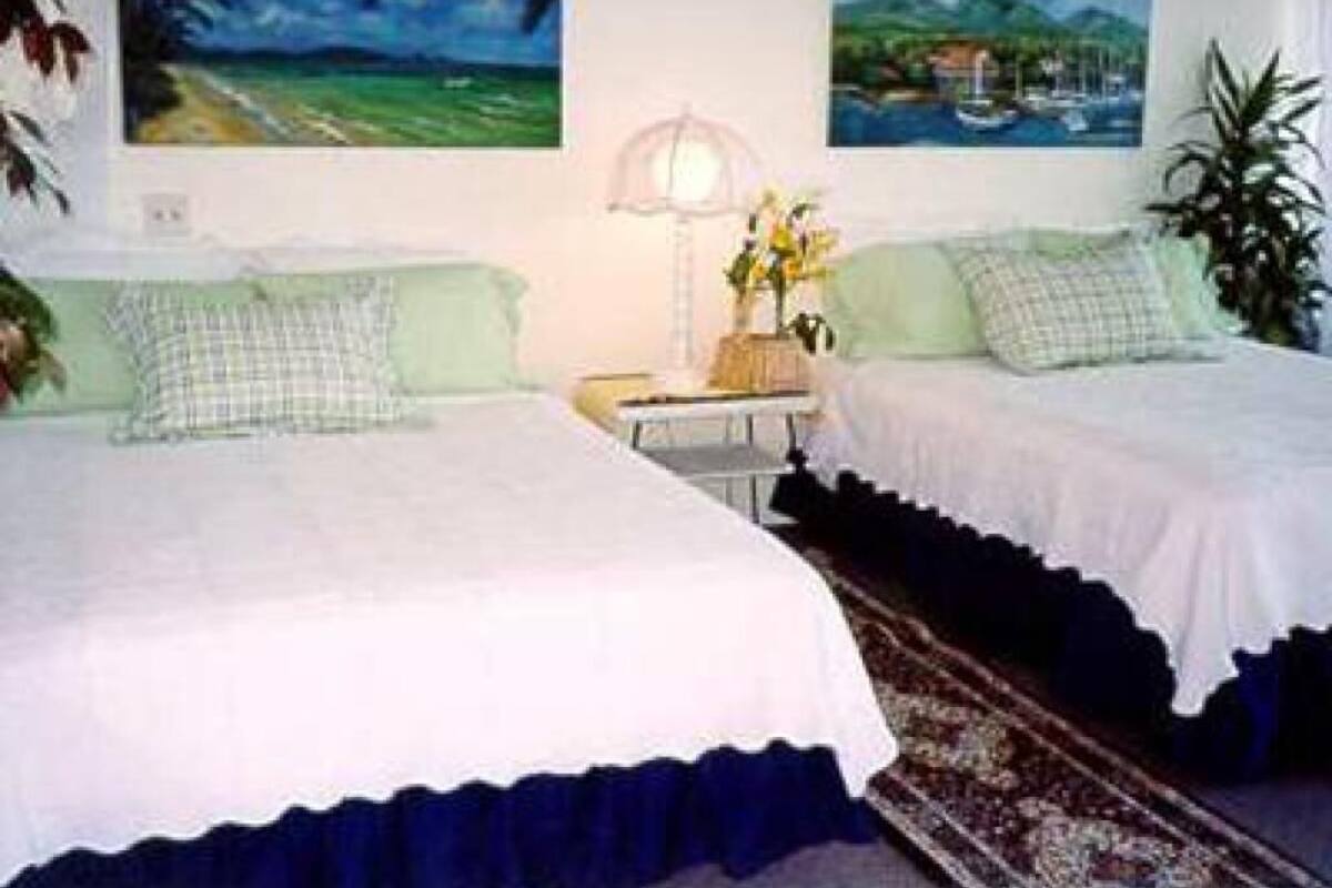 A room with two beds, a nightstand with a lamp, and two paintings on the wall.