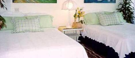 A room with two beds, a nightstand with a lamp, and two paintings on the wall.